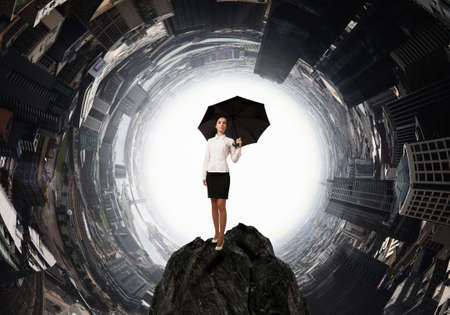 Young businesswoman with black umbrella standing on topの写真素材
