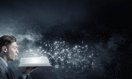 Young businessman with opened book in hands blowing on pages
