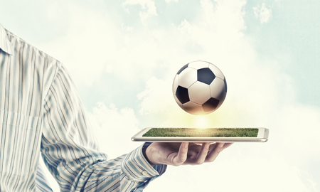 Tablet pc in male hand and soccer ball on screenの写真素材