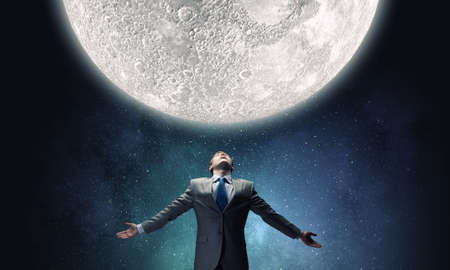 Businessman with hands spread apart looking at moon aboveの写真素材