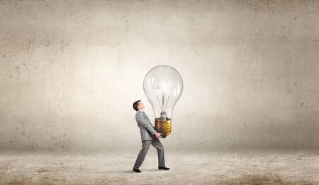 Young businessman carrying big light bulb in handsの写真素材