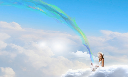 Young lady sitting on cloud with laptop on kneesの写真素材