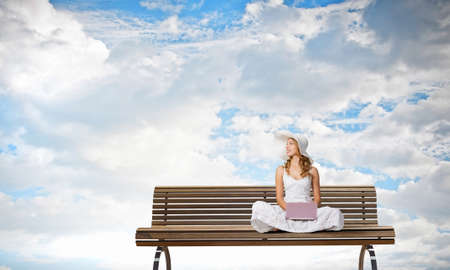 Young lady sitting on bench and using laptopの写真素材