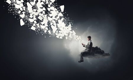 Young businessman sitting on cloud with mobile phone in handsの写真素材