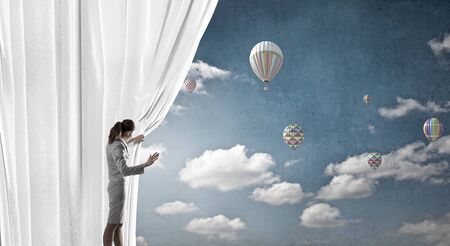 Young businesswoman opening stage curtain to another realityの写真素材