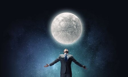 Businessman with hands spread apart looking at moon aboveの写真素材