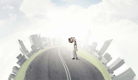 Woman with suitcase in white long dress and hat on asphalt  roadの写真素材