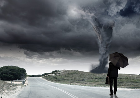 Back view of businessman with umbrella and suitcase facing tornado