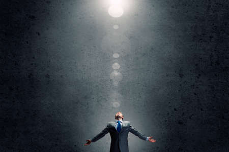 Businessman with hands spread apart standing in light coming from aboveの写真素材