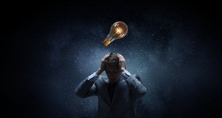 Depressed businessman and glowing idea bulb above his headの写真素材
