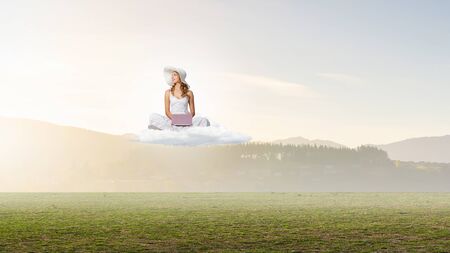 Young lady sitting on cloud and using laptopの写真素材