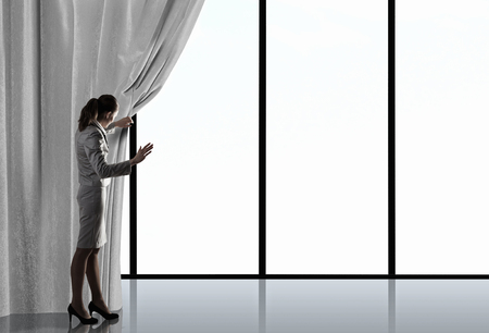 Businesswoman pulling curtain and cityscape behind itの写真素材