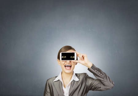 Beautiful young woman holding mobile phone against her eyesの写真素材