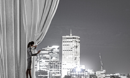 Businesswoman pulling curtain and cityscape behind itの写真素材