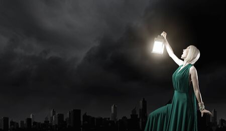 Young attractive woman in green dress with lantern walking in darknessの写真素材