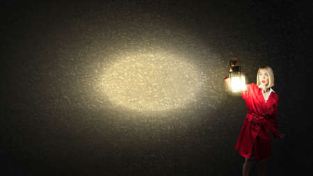 Young blond woman in red cloak with lantern lost in darknessの写真素材