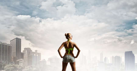 Rear view of young pretty woman in bikini and shorts with shopping bagsの写真素材