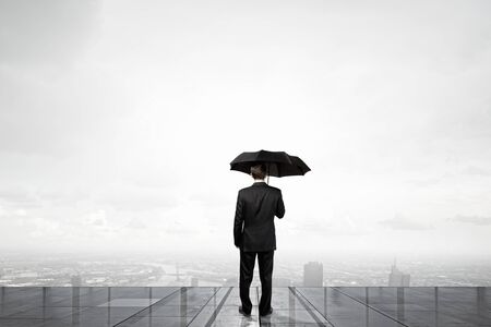 Back view of businessman with umbrella looking at cityの写真素材