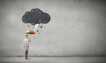 Young businesswoman with colorful umbrella under black cloudの写真素材