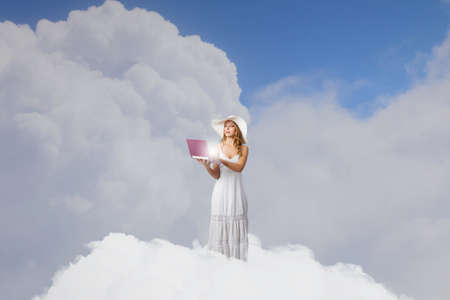 Young lady standing on cloud and using laptopの写真素材