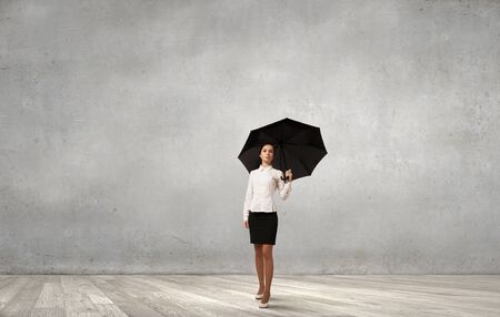 Young businesswoman with black umbrella standing under black cloudの写真素材