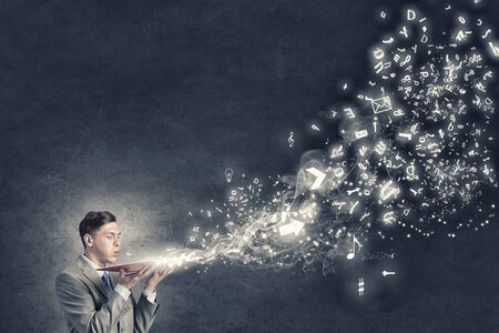 Young businessman with opened book in hands blowing on pagesの写真素材