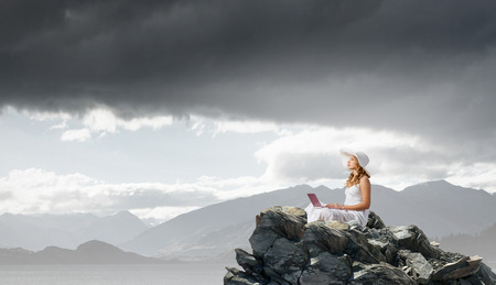 Young lady sitting on top of mountain with laptopの写真素材