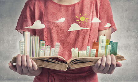 Young woman in red dress holding opened book with city modelの写真素材