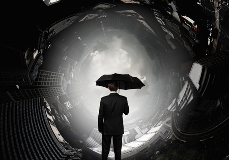Back view of businessman with umbrella looking at cityの写真素材