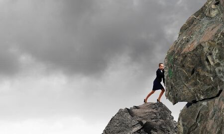Young businesswoman making effort to move huge stoneの写真素材