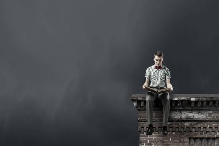 Young man in bow tie sitting with book in handsの写真素材