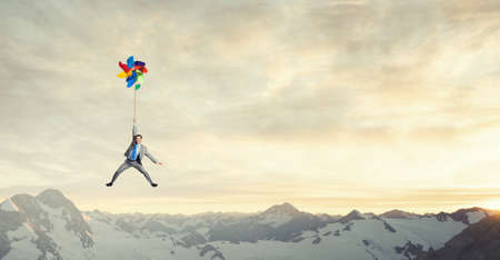 Young happy businessman flying in sky on colorful windmillの写真素材