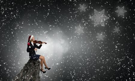 Woman in formal suit and Santa hat playing violinの写真素材