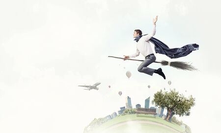 Young businessman flying on broom high in skyの写真素材