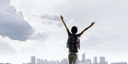 Back view of cheerful woman with hands up facing sunriseの写真素材