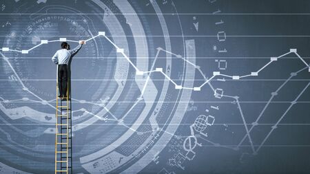 Back view of businessman standing on ladder and drawing sketch on wallの写真素材