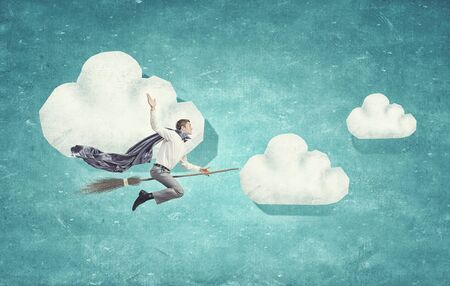 Young businessman flying on broom high in skyの写真素材