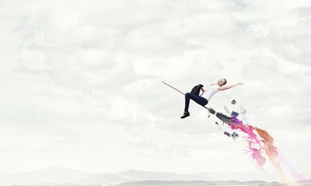 Happy young woman flying in sky on broomの写真素材