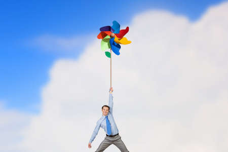 Young happy businessman flying in sky on colorful windmillの写真素材