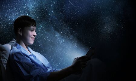 Young teenager guy in bed using tablet pcの写真素材