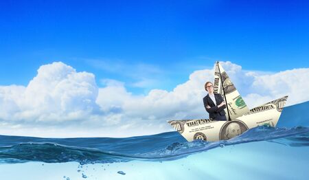 Businesswoman escapes from crisis on paper boat made of dollar banknoteの写真素材