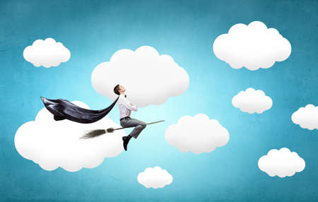Young businessman flying on broom high in skyの写真素材