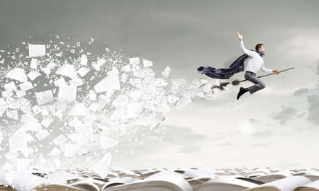 Young businessman flying on broom high in skyの写真素材