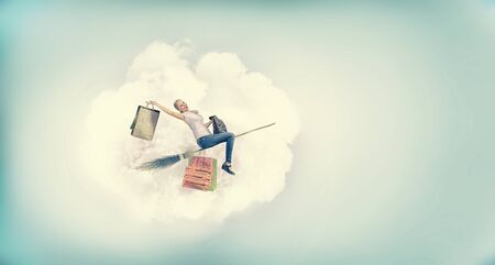 Happy young woman flying in sky on broomの写真素材