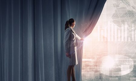 Young businesswoman opening curtain and presenting digital financial infographsの写真素材