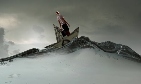 Businesswoman escapes from crisis on paper boat made of dollar banknoteの写真素材