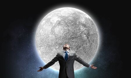 Businessman with hands spread apart looking at moon aboveの写真素材