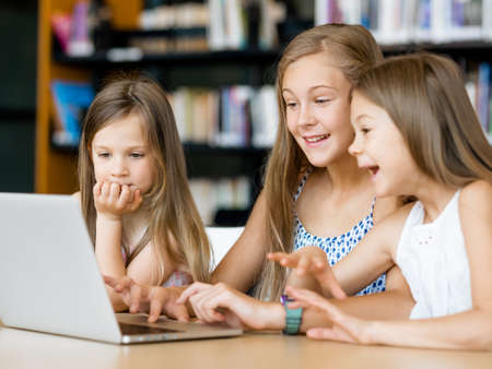 Little girls with a laptop in libraryの写真素材