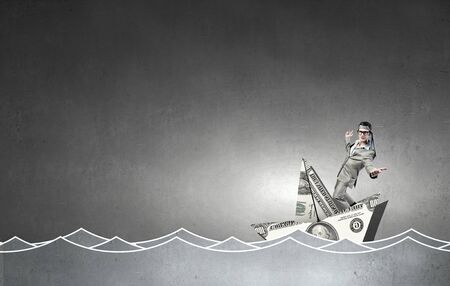 Businessman escapes from crisis on paper boat made of dollar banknoteの写真素材