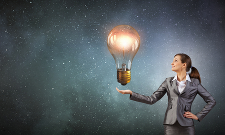 Young businesswoman presenting glass glowing light bulb in her handの写真素材